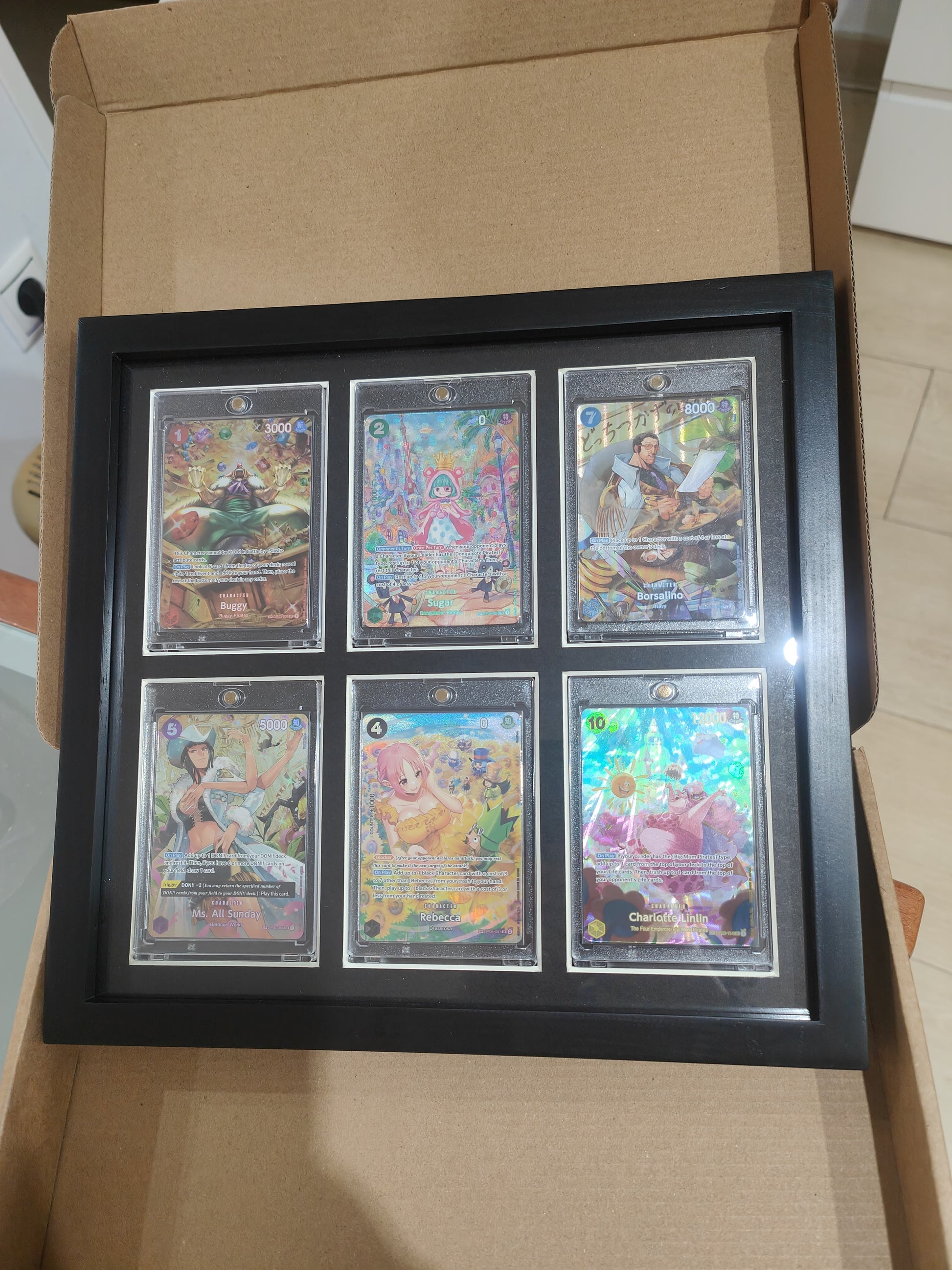 Se ve el marco ya montado con sus toploaders y 6 cartas dentro en dos filas de 3 y 3